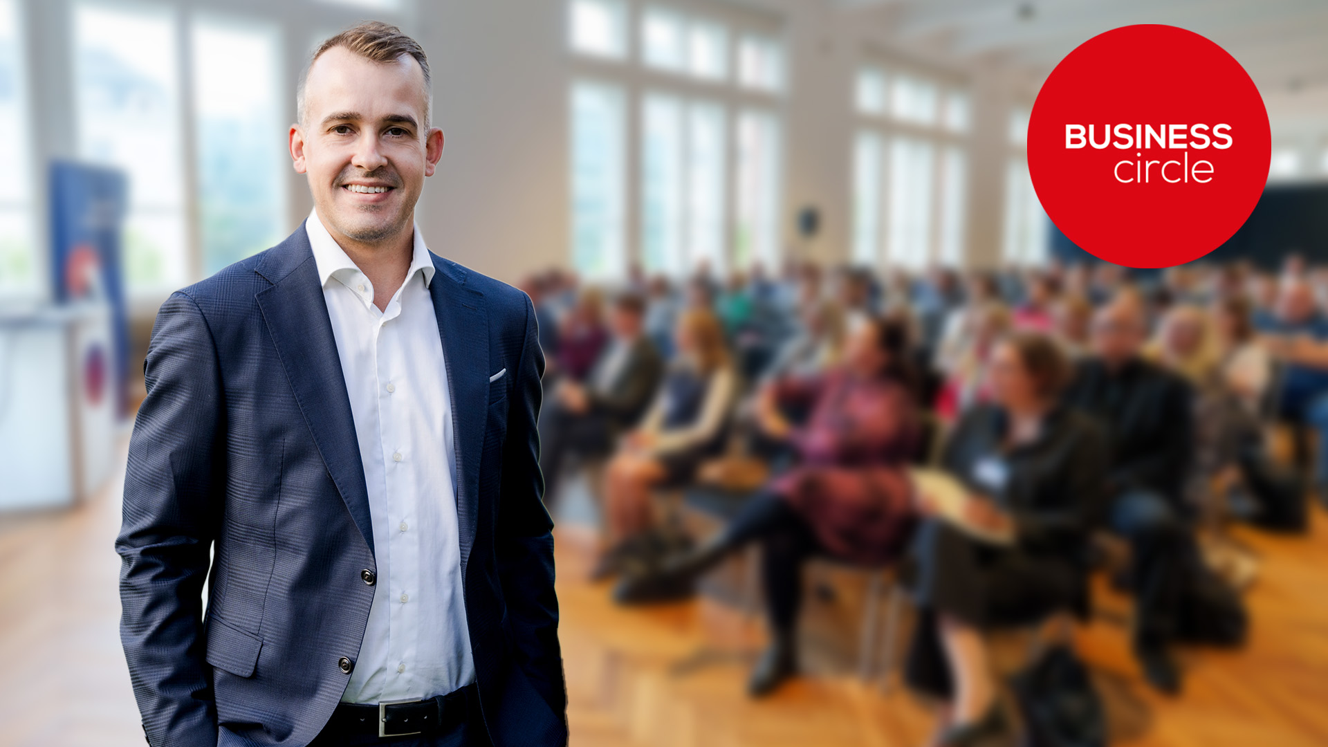 Rechtsanwalt Berthold Hofbauer steht links im Bild. Dahinter als Hintergrund ist ein Publikum. Oben rechts ist das Business Circle Logo.